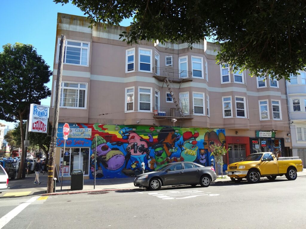 Building with colorful mural and parked cars on street.